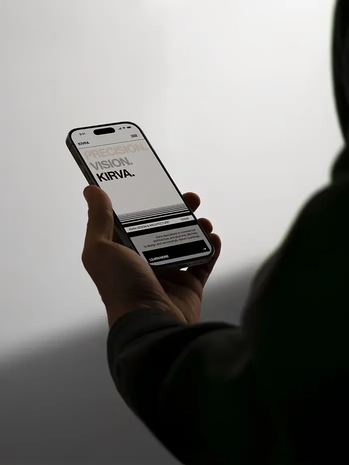 Person holding a smartphone displaying a webpage with the text 'PRECISION. VISION. KIRVA.' and a section about Kirva Design Architecture.