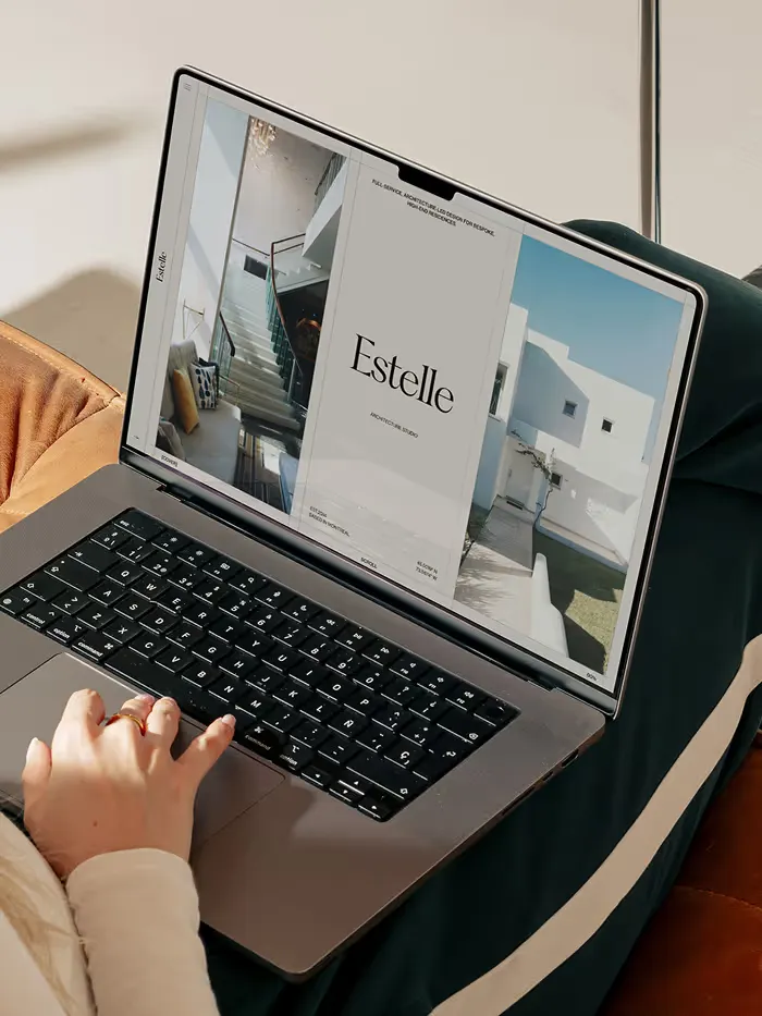 Person using a laptop showing an architectural design portfolio titled 'Estelle' with interior and exterior houses.
