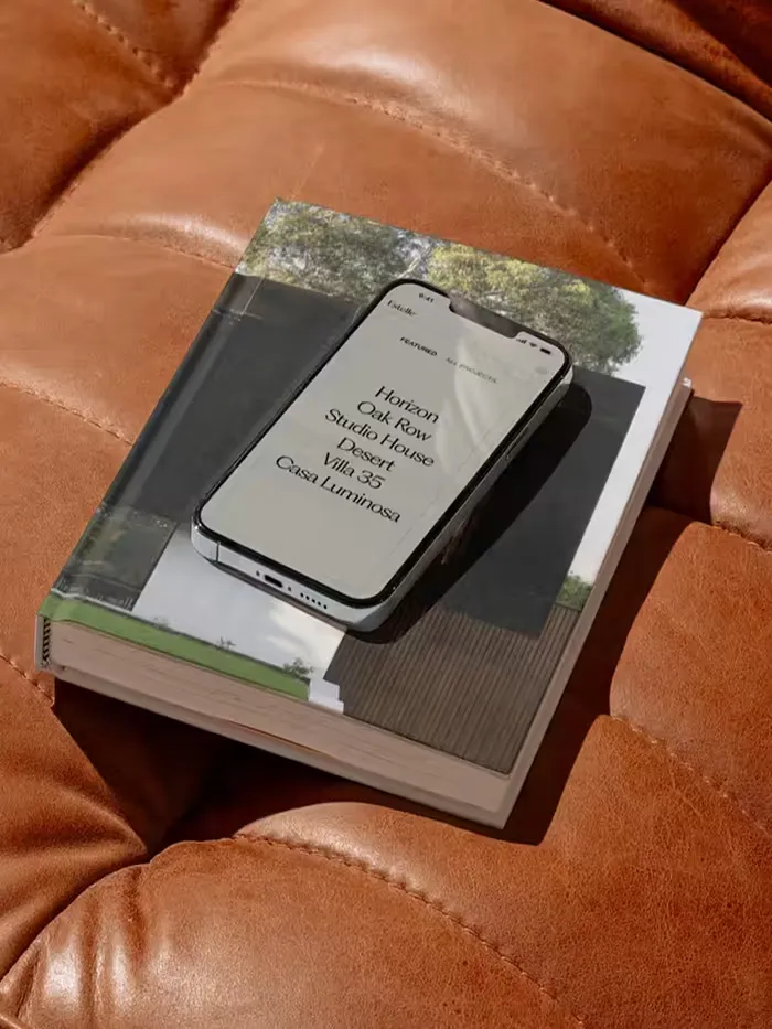 Smartphone displaying a list of project names resting on an architectural book on a brown leather surface.