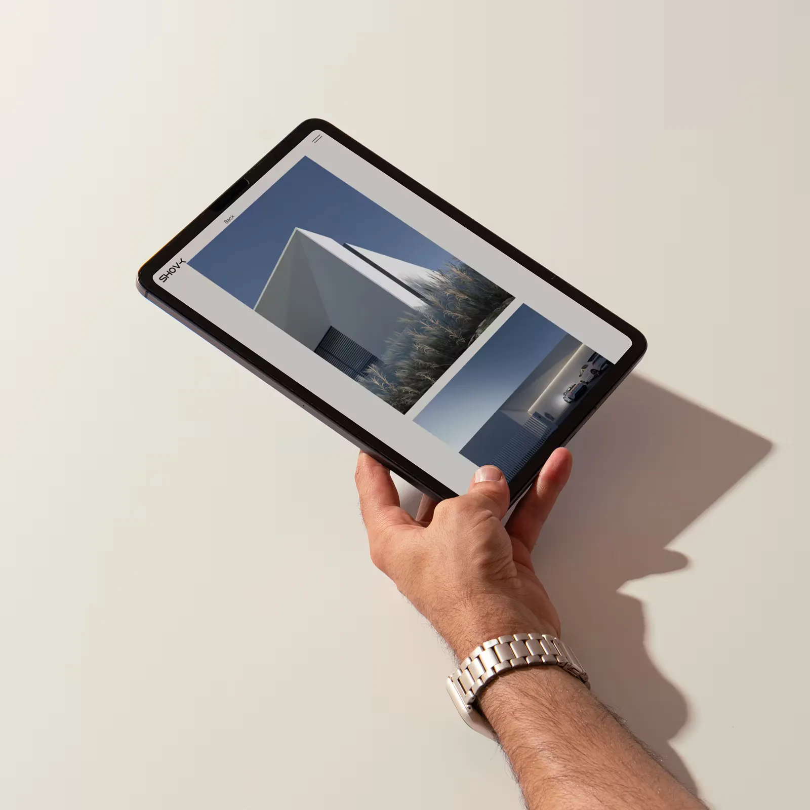Hand holding a tablet displaying a modern white building against a blue sky.