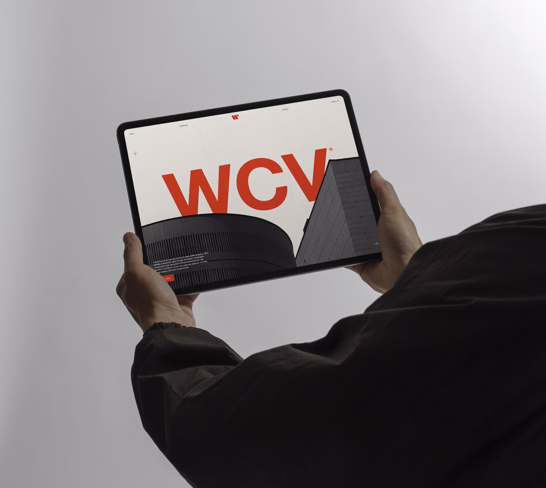Hands holding a tablet displaying a website with large red letters WCV and images of modern buildings.