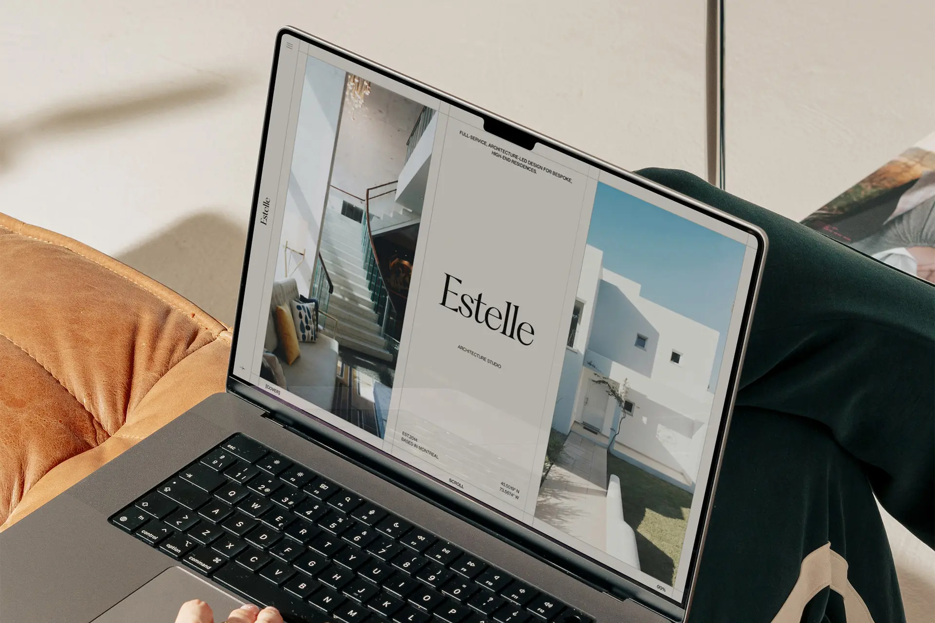 Laptop displaying the Estelle architecture studio website, featuring a split-screen layout with an interior staircase and a modern white building, set on a tan leather sofa.