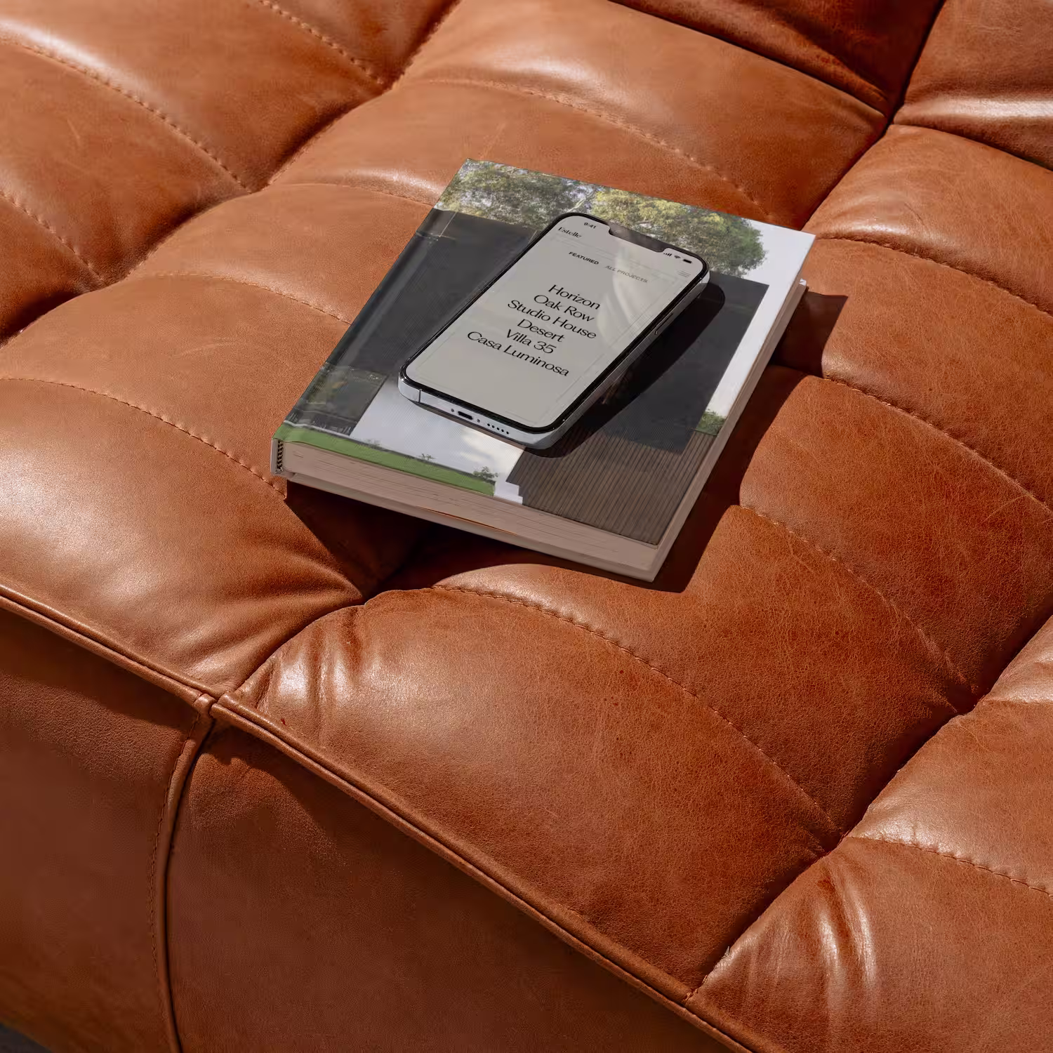 Smartphone showing the Estelle architecture studio project page placed on top of an architecture book on a tan leather sofa.
