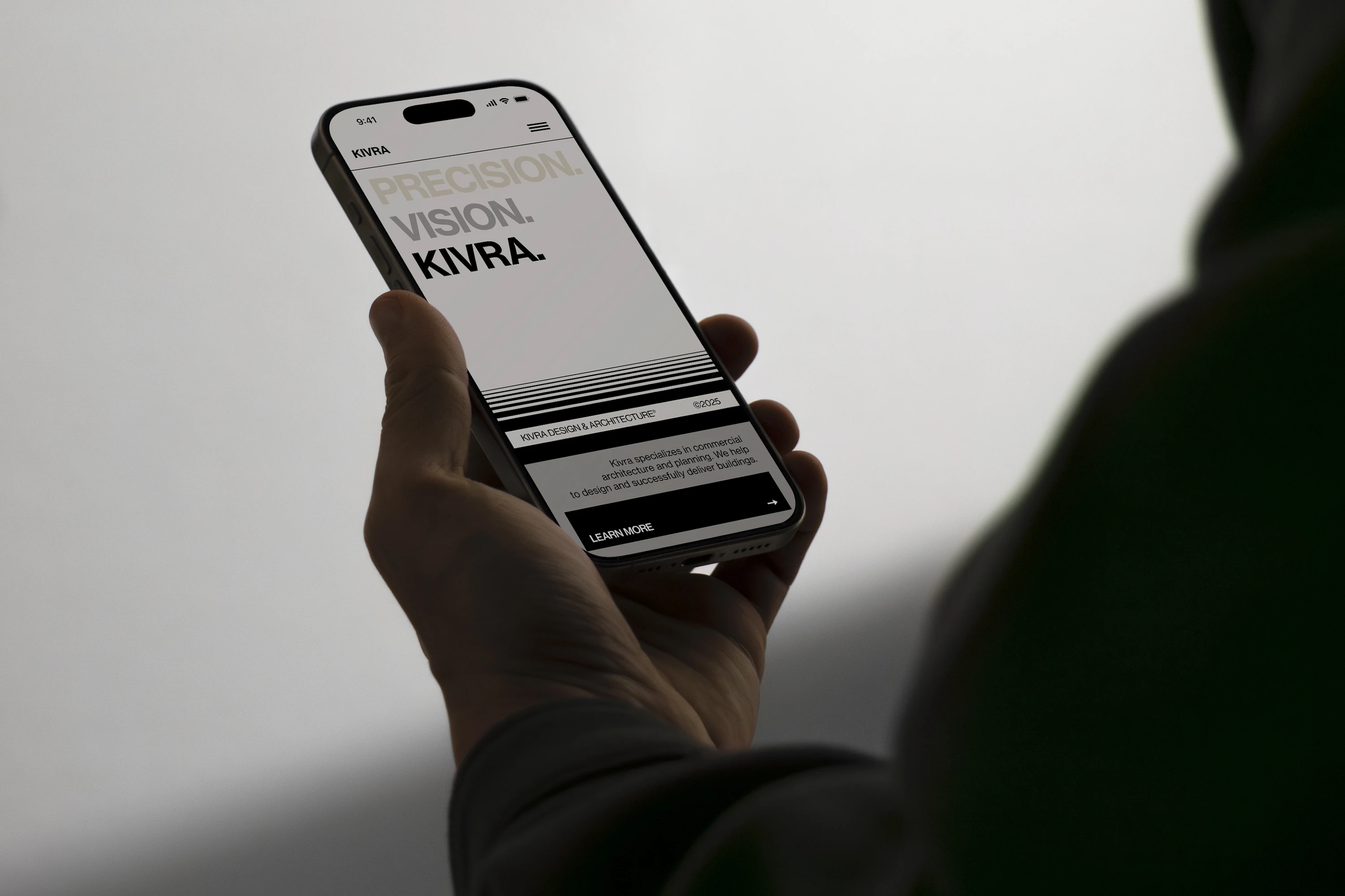 Person holding a smartphone showing the mobile version of the KIVRA architecture studio homepage with strong branding and tagline.